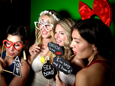 Η νύφη με τις φίλες της φωτογραφίζονται κρατώντας props και παιχνίδια σε γαμήλιο πάρτυ με το Smileme photobooth στους Παξούς